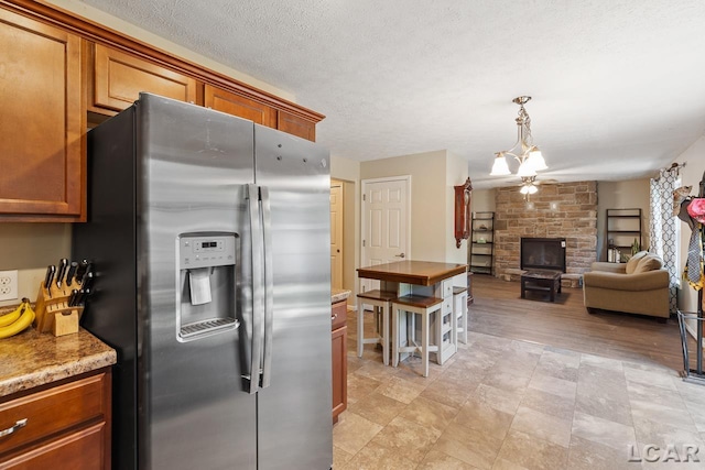 kitchen with stainless steel fridge, a stone fireplace, a textured ceiling, and light hardwood / wood-style flooring