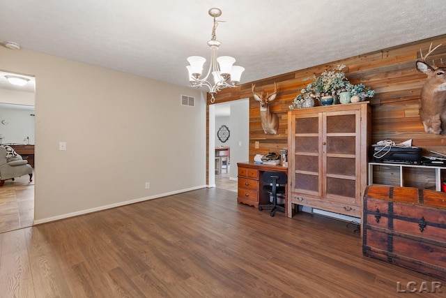 office space with a chandelier, dark wood-type flooring, and wood walls