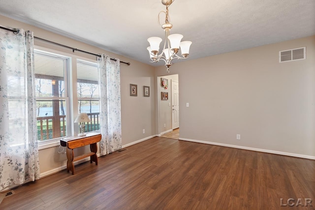 empty room with a textured ceiling, dark hardwood / wood-style floors, and an inviting chandelier