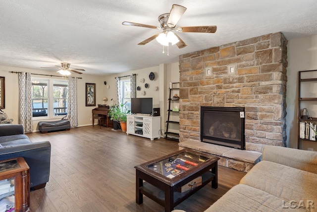 living room with a stone fireplace, plenty of natural light, dark wood-type flooring, and a textured ceiling