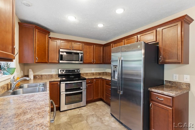 kitchen with a textured ceiling, stainless steel appliances, light stone counters, and sink