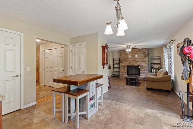 dining area featuring a fireplace, a textured ceiling, ceiling fan with notable chandelier, and light hardwood / wood-style flooring