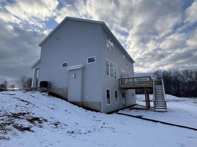 snow covered back of property featuring central air condition unit and a deck