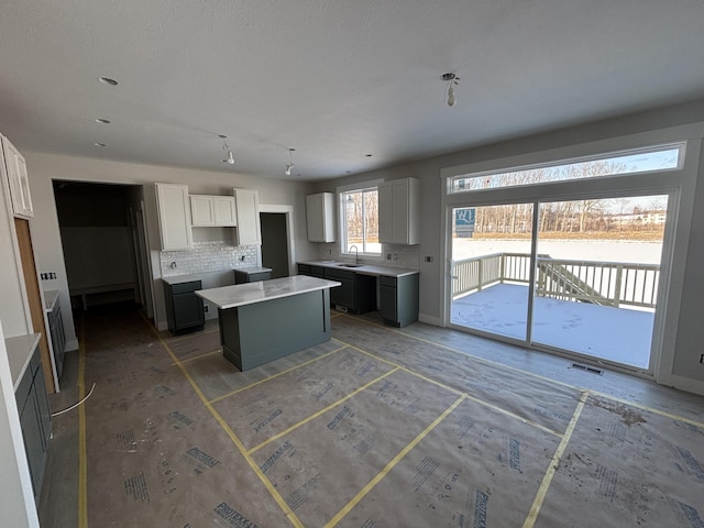 kitchen with backsplash, sink, a kitchen island, and white cabinets