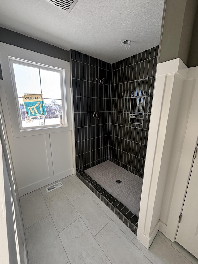 bathroom with tile patterned flooring, a textured ceiling, and tiled shower