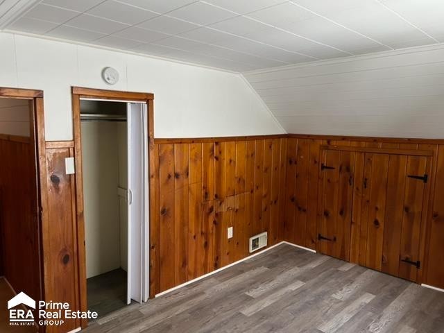 additional living space featuring hardwood / wood-style floors, vaulted ceiling, and wooden walls