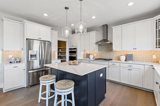 kitchen with a kitchen island, wall chimney exhaust hood, stainless steel appliances, and light wood-type flooring