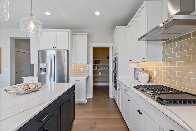 kitchen featuring tasteful backsplash, stainless steel appliances, wall chimney range hood, pendant lighting, and light hardwood / wood-style flooring