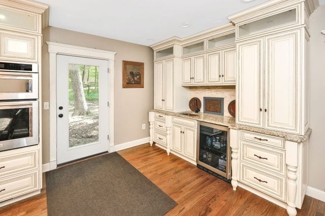 kitchen with cream cabinetry, double oven, beverage cooler, and dark hardwood / wood-style floors