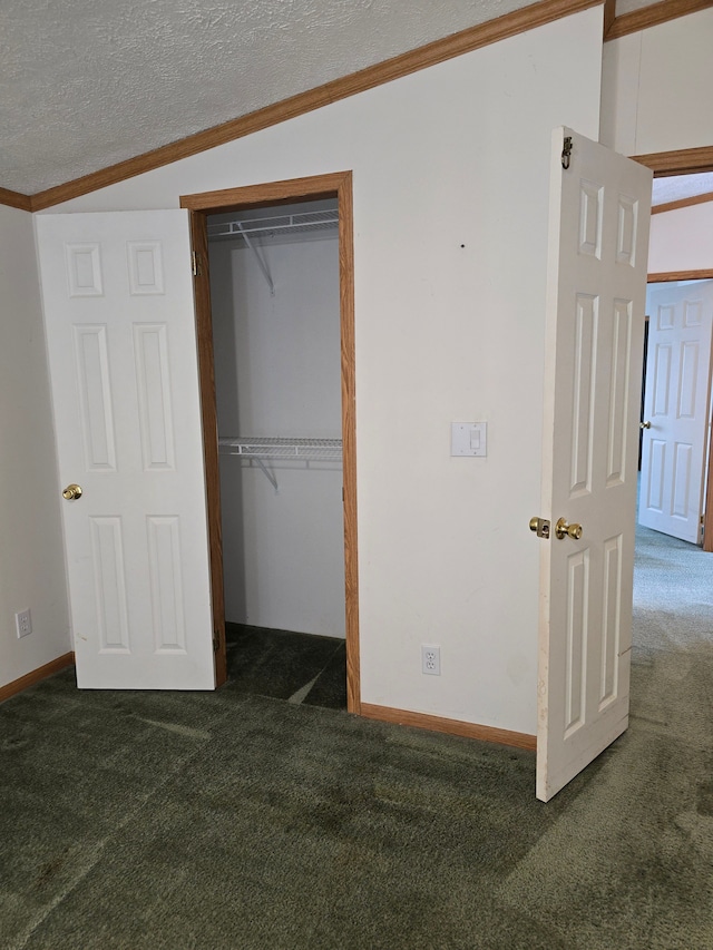 unfurnished bedroom featuring lofted ceiling, crown molding, a textured ceiling, a closet, and dark colored carpet