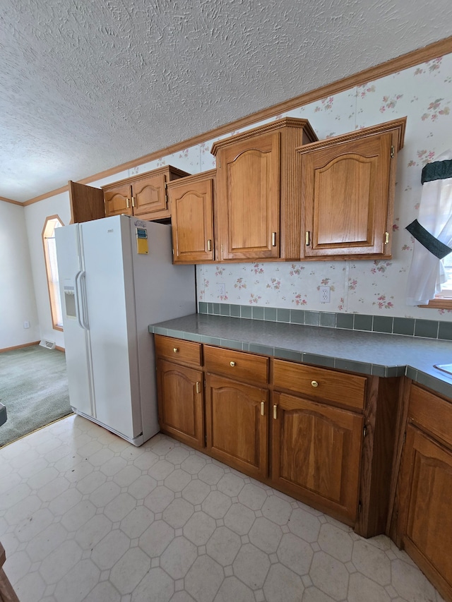 kitchen with a textured ceiling, ornamental molding, tile countertops, and white fridge with ice dispenser