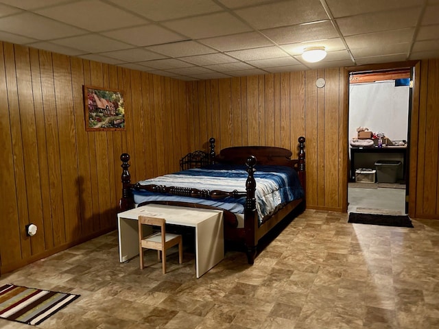 bedroom featuring baseboards, a drop ceiling, and wooden walls