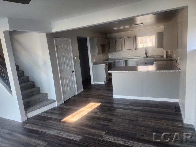 kitchen featuring dark wood-type flooring, a sink, a peninsula, and baseboards