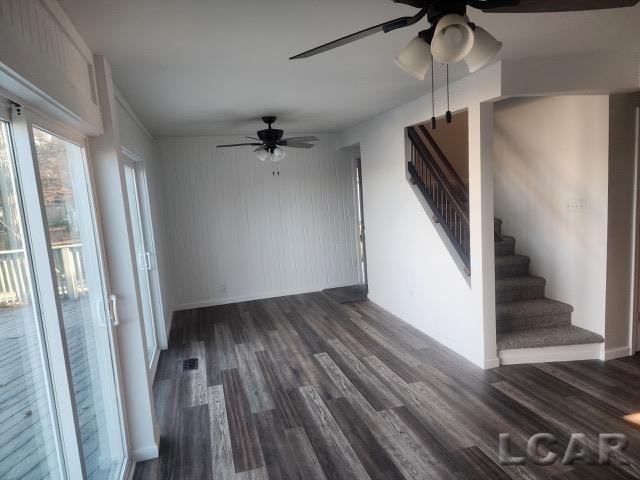 unfurnished room with stairs, dark wood-style flooring, visible vents, and a ceiling fan