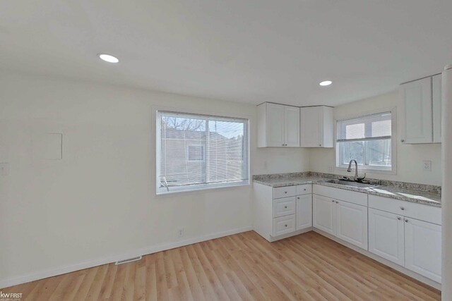 kitchen featuring white cabinets, light stone counters, light hardwood / wood-style flooring, and sink