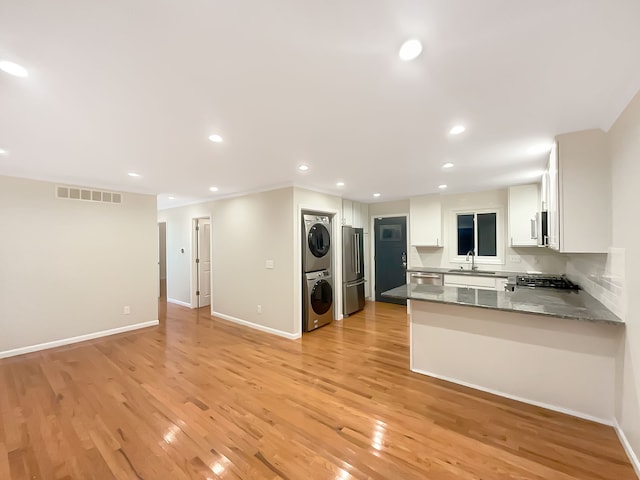 kitchen featuring kitchen peninsula, stacked washer and dryer, light hardwood / wood-style flooring, appliances with stainless steel finishes, and white cabinetry