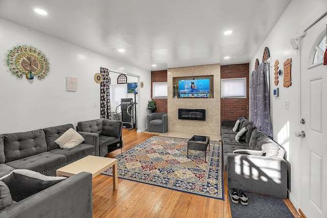 living room featuring a tiled fireplace, wood-type flooring, and brick wall