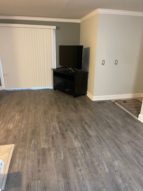 unfurnished living room featuring ornamental molding and dark wood-type flooring