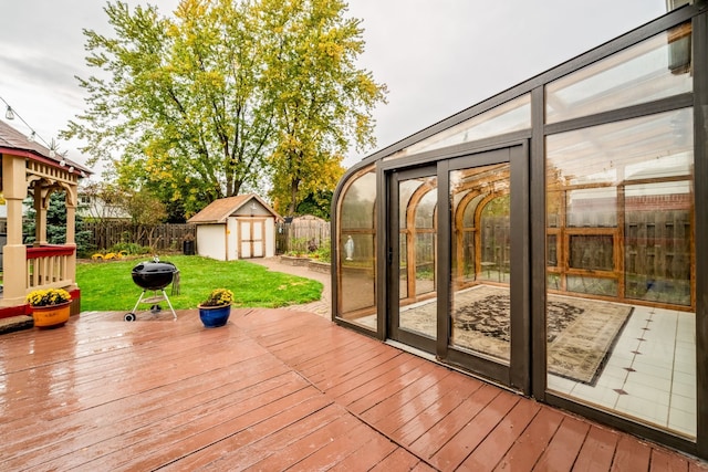 wooden terrace with a sunroom, area for grilling, a storage shed, and a lawn