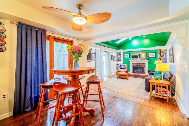 dining area with ceiling fan, wood-type flooring, lofted ceiling, a tray ceiling, and a fireplace