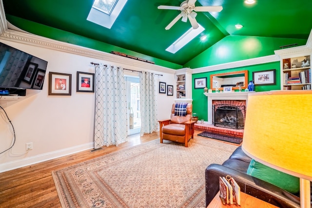 sitting room featuring a fireplace, ceiling fan, vaulted ceiling with skylight, and hardwood / wood-style floors