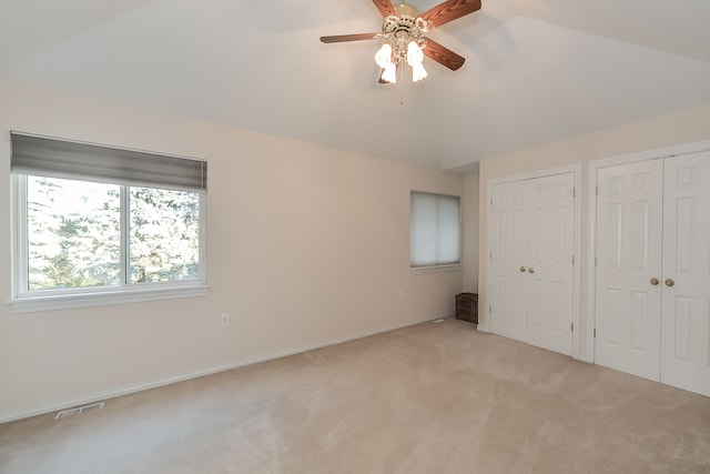 unfurnished bedroom with light carpet, vaulted ceiling, ceiling fan, and multiple closets