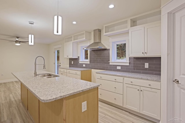 kitchen featuring pendant lighting, a kitchen island with sink, sink, light hardwood / wood-style flooring, and wall chimney exhaust hood