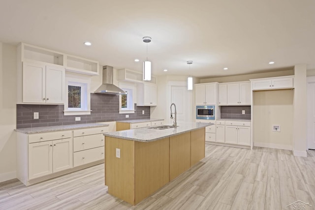 kitchen featuring sink, white cabinetry, a kitchen island with sink, and wall chimney range hood