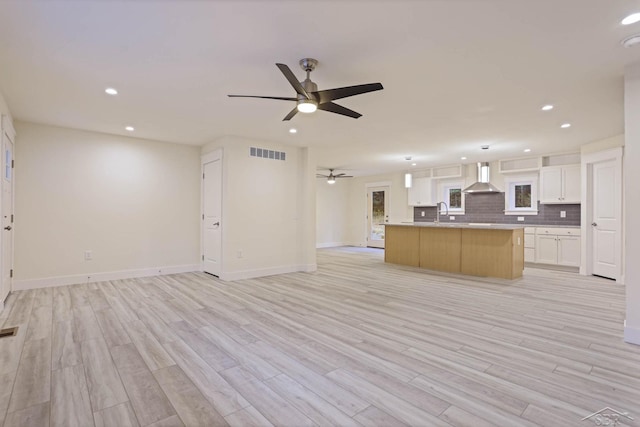 kitchen featuring white cabinetry, a center island, wall chimney range hood, and light wood-type flooring