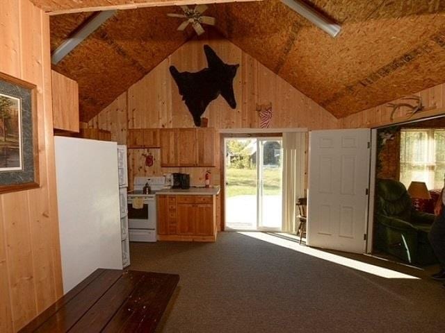 kitchen featuring ceiling fan, carpet floors, vaulted ceiling, white appliances, and wooden walls