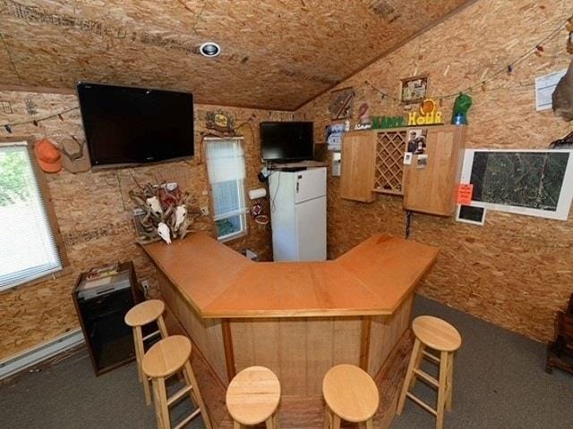 bar with white refrigerator and vaulted ceiling