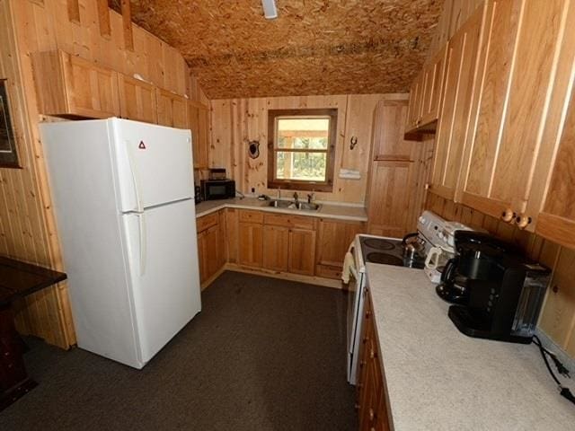 kitchen featuring dark carpet, white appliances, sink, wooden walls, and vaulted ceiling