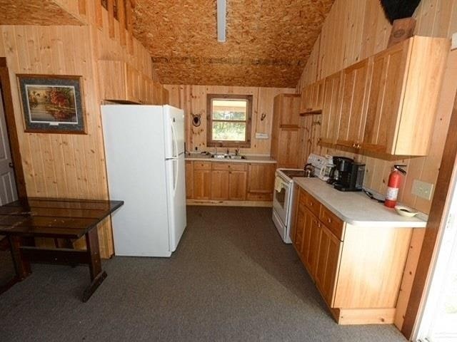 kitchen featuring wooden walls, dark carpet, and white appliances