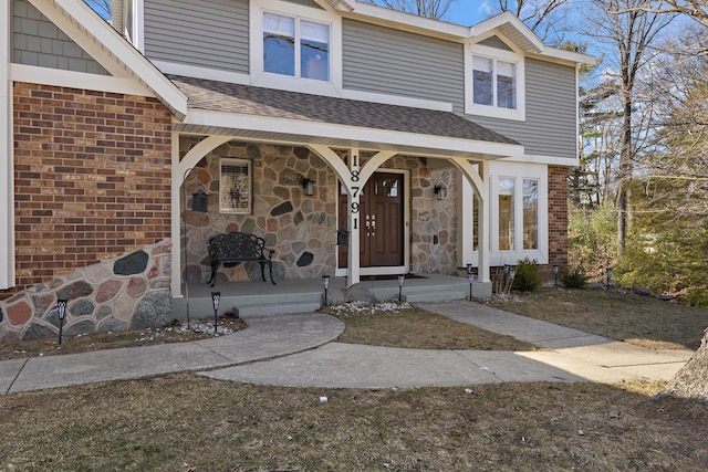 entrance to property with stone siding, brick siding, a porch, and roof with shingles