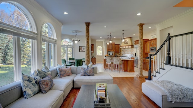 living room with light hardwood / wood-style flooring, ornate columns, ornamental molding, and a notable chandelier