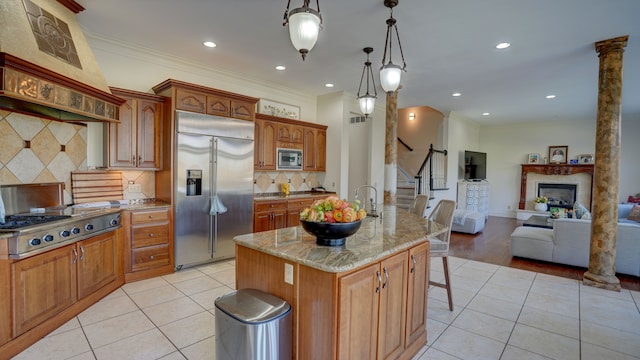 kitchen with custom exhaust hood, a center island with sink, crown molding, built in appliances, and decorative light fixtures