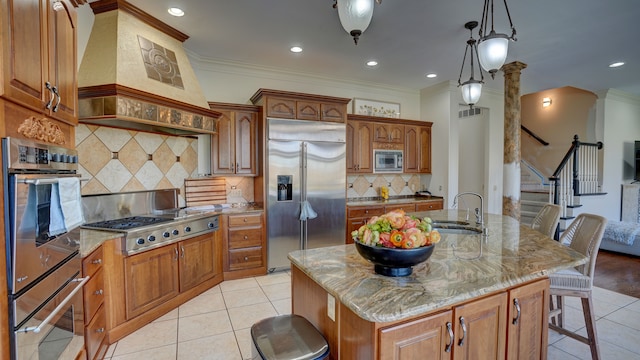 kitchen with light stone countertops, sink, built in appliances, a breakfast bar area, and an island with sink