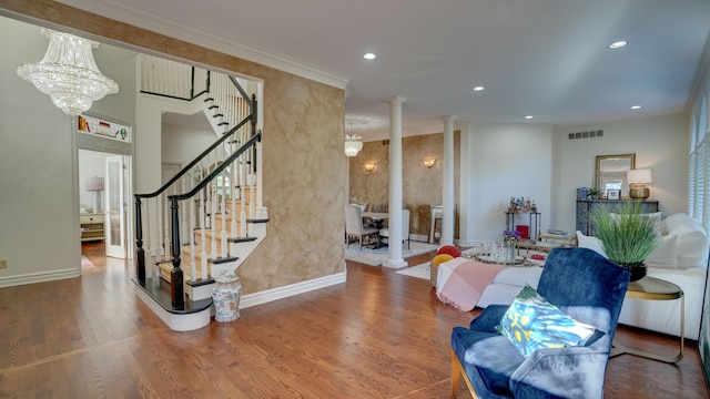 living room with decorative columns, wood-type flooring, ornamental molding, and a chandelier