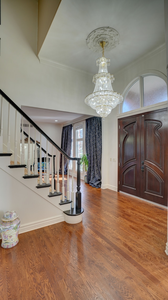 entrance foyer with wood-type flooring, crown molding, and a chandelier