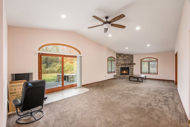 carpeted office with a stone fireplace, ceiling fan, a healthy amount of sunlight, and lofted ceiling