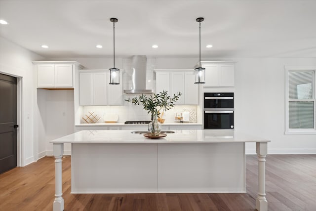 kitchen with appliances with stainless steel finishes, hanging light fixtures, a center island with sink, and wall chimney range hood