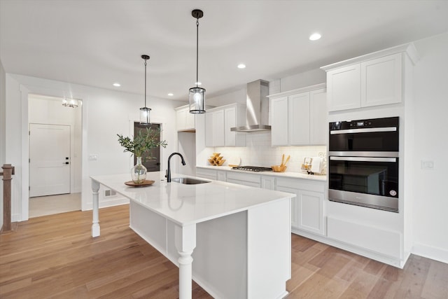 kitchen featuring hanging light fixtures, white cabinets, an island with sink, and wall chimney exhaust hood