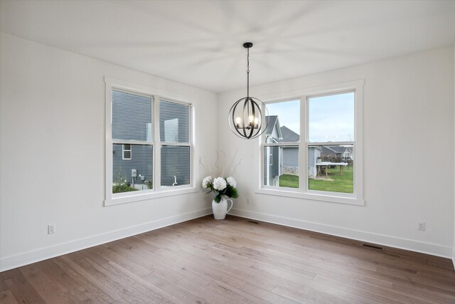 unfurnished dining area featuring an inviting chandelier and hardwood / wood-style floors