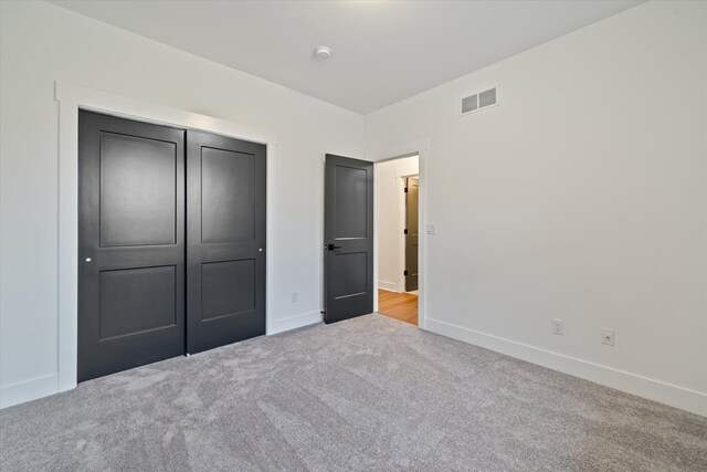 unfurnished bedroom with light carpet and a closet