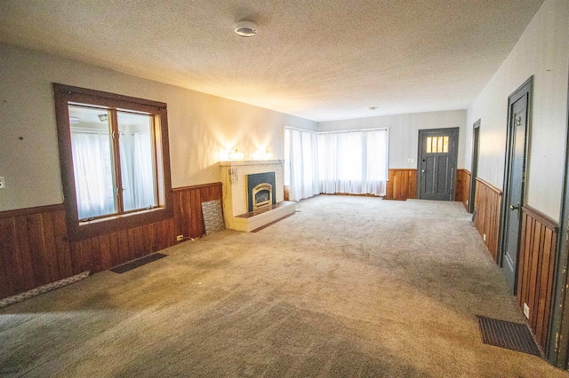 unfurnished living room with carpet, a textured ceiling, and wooden walls