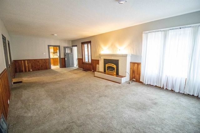 unfurnished living room with a textured ceiling, a tile fireplace, carpet floors, and wooden walls