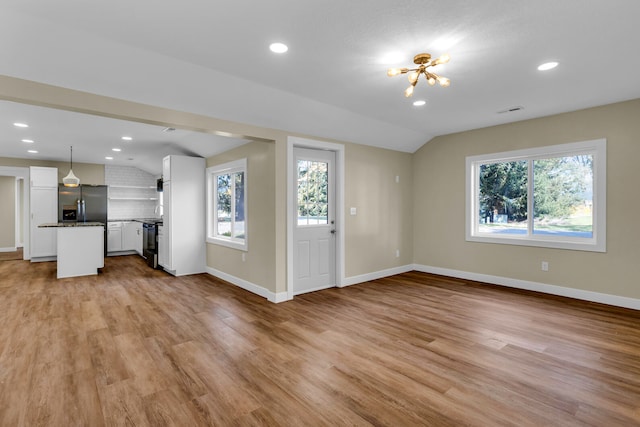 unfurnished living room featuring an inviting chandelier, light wood-type flooring, and vaulted ceiling