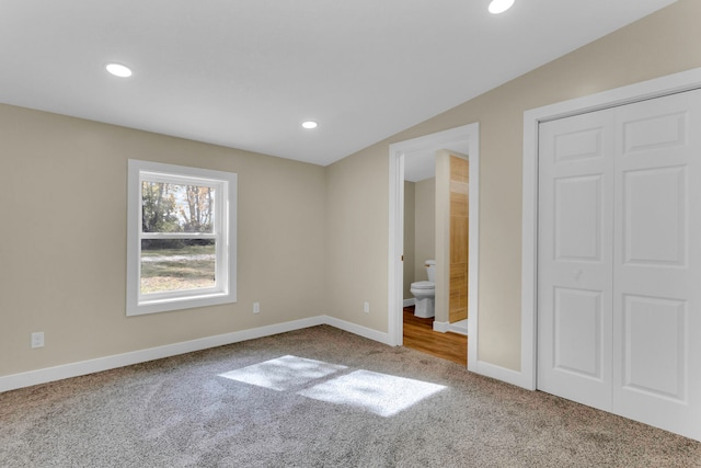 unfurnished bedroom with carpet flooring, ensuite bath, a closet, and lofted ceiling