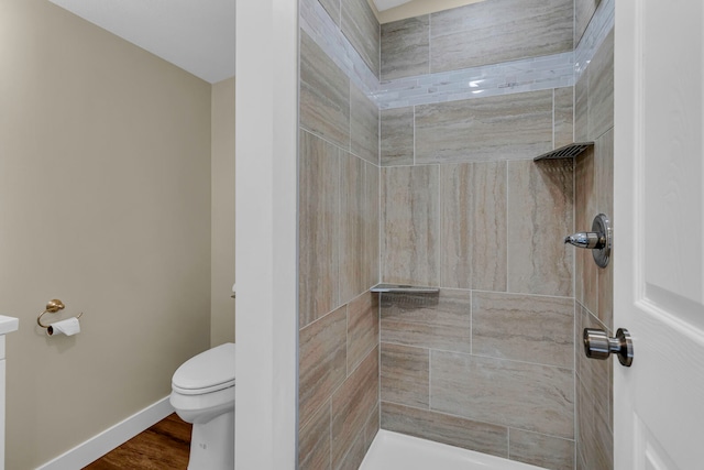 bathroom with hardwood / wood-style floors, toilet, and a tile shower