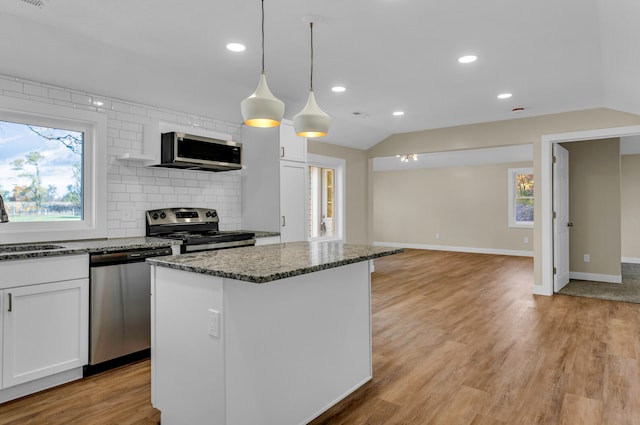 kitchen with dark stone counters, white cabinets, light hardwood / wood-style flooring, appliances with stainless steel finishes, and decorative light fixtures